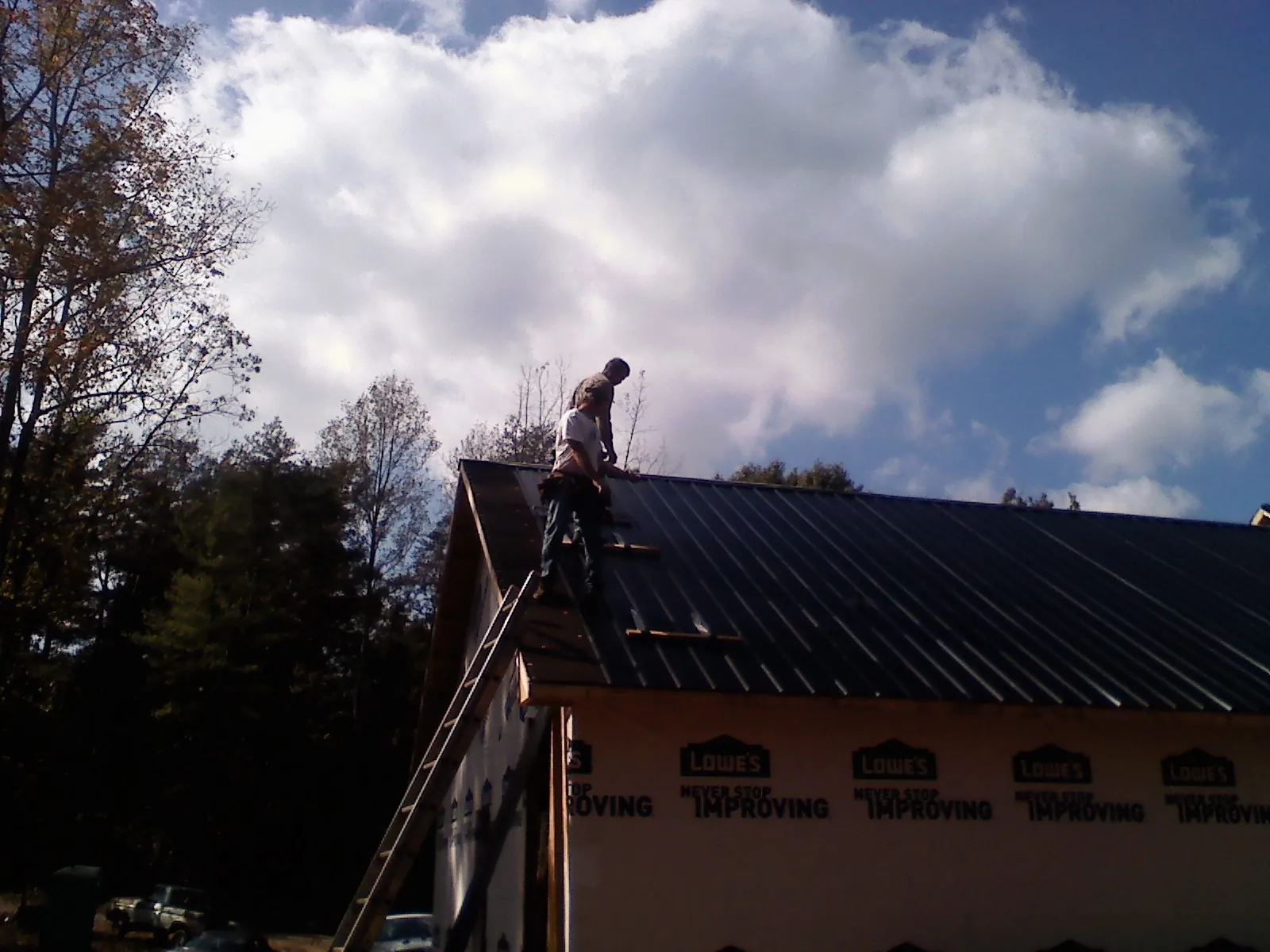 Roofer fastening dark metal panels high against a cloudy sky, from a Roof Inspection job in Vandalia